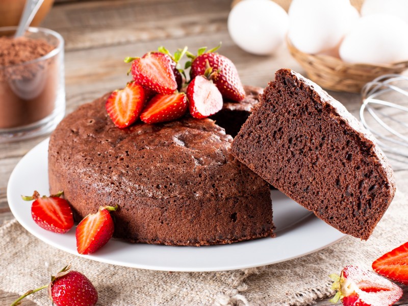 3-Zutaten-Schokokuchen dekoriert mit Erdbeeren, aus dem ein Stück herausguckt.