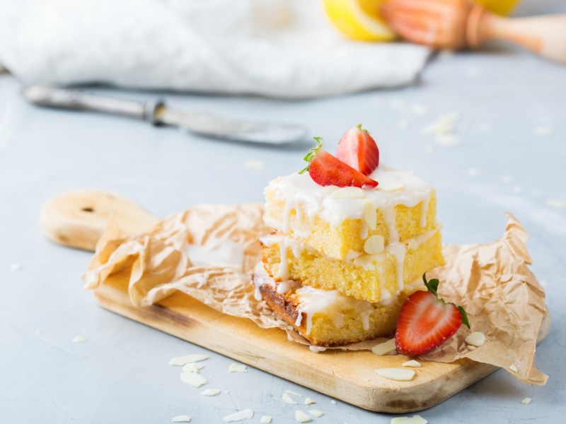 3 Stücke Aperol-Spritz-Kuchen gestapelt mit Zuckerguss auf einem Holzbrett, mit Erdbeeren garniert.