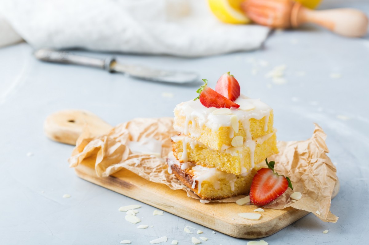 3 Stücke Aperol-Spritz-Kuchen gestapelt mit Zuckerguss auf einem Holzbrett, mit Erdbeeren garniert.