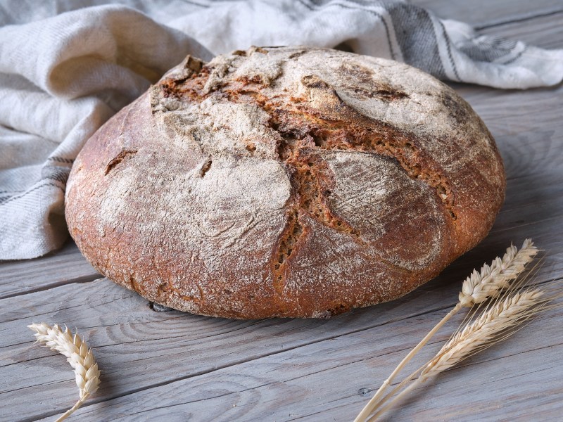 Bauernbrot auf einem Tisch, daneben liegen Weizenähren.