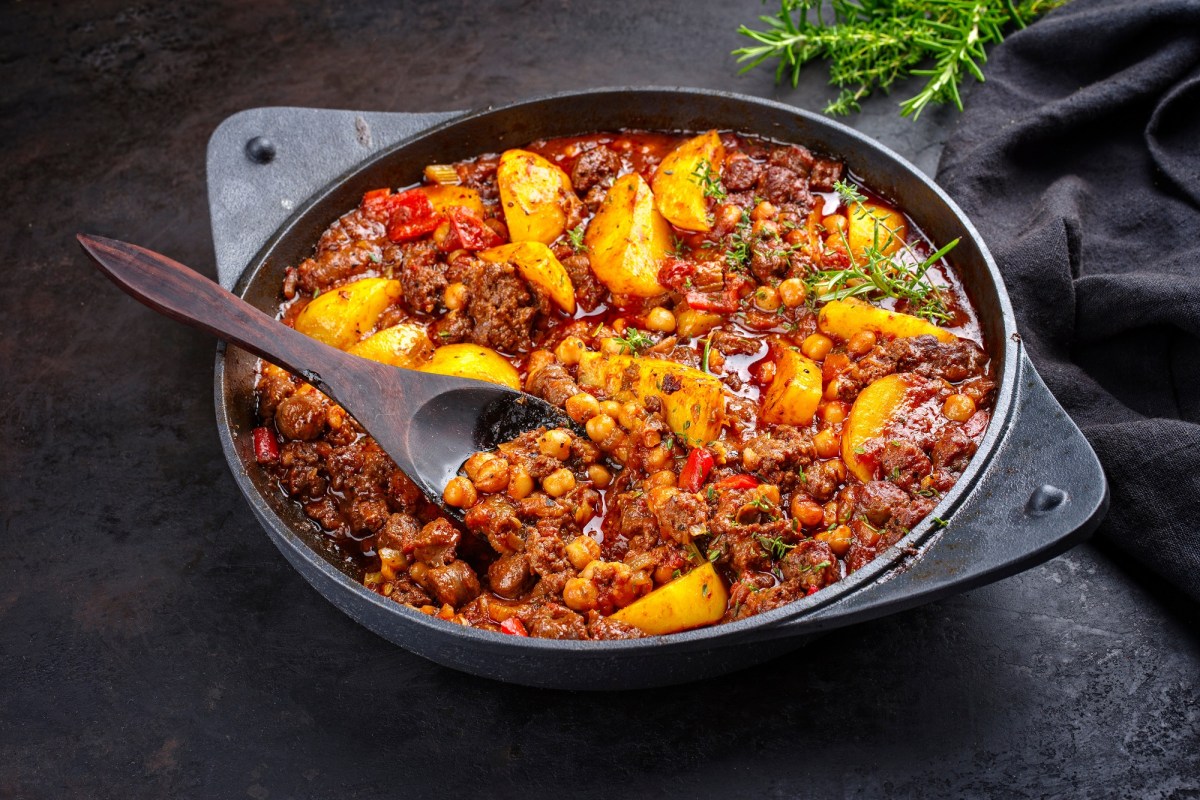 Bauerntopf mit Hackfleisch, Kartoffeln, Paprika und mehr Gemüse in einer tiefen Pfanne, darin ein Holzlöffel, Nahaufnahme.