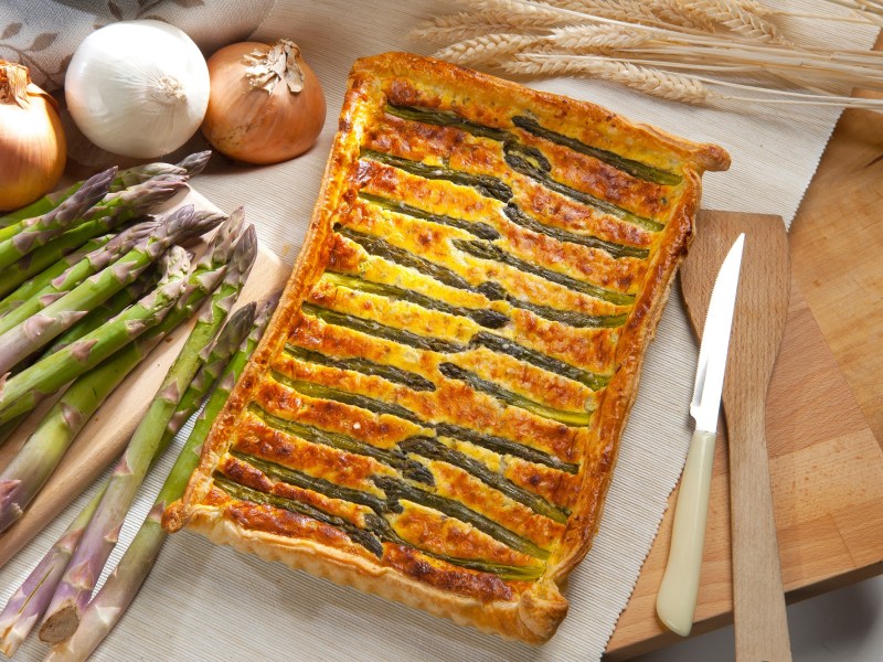 Blätterteigtarte mit Spargel und Parmesan auf einem dekorierten Tisch.