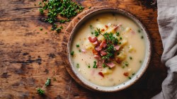 Schale mit einer Bratkartoffelsuppe mit Speck auf Holztisch.