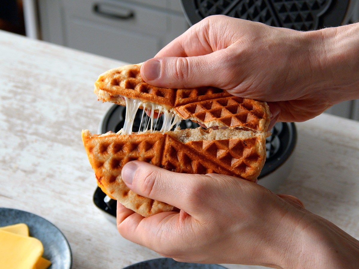 Gefülltes Brötchen im Waffeleisen wird von zwei Händen auseinander gebrochen.