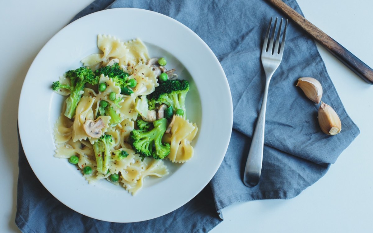 Ein Teller mit Brokkoli-Champignon-Pasta mit Erbsen. Daneben liegt Besteck.