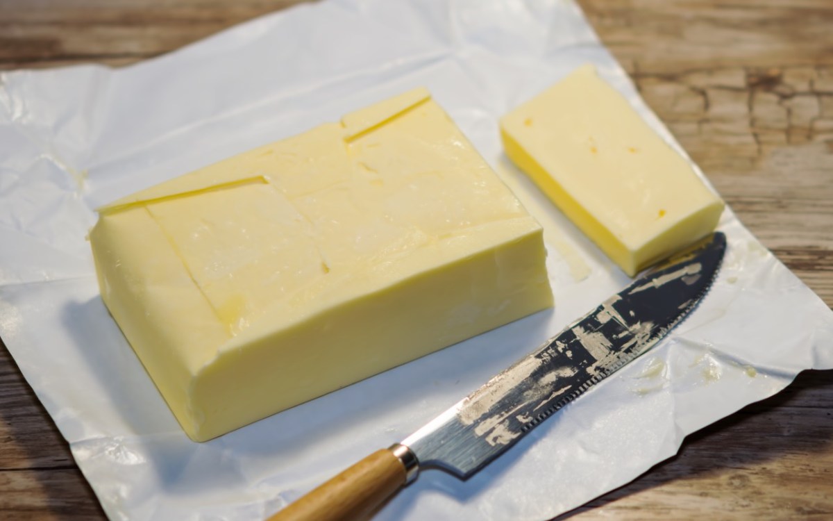 Ein Stück eingefrorene Butter, von dem mit einem Messer eine Scheibe abgeschnitten wurde.