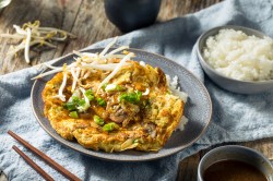 Teller mit Egg Foo Yung und einer Schale Reis auf Tischdecke