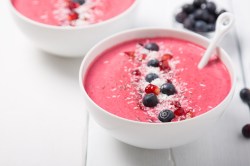 2 Erdbeer-Smoothie-Bowls garniert mit Blaubeeren, Kokosflocken und Granatapfelkernen.