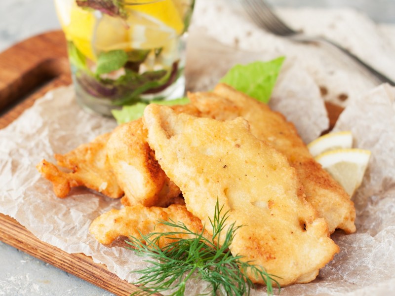 Fisch in Bierteig auf Backpapier mit Kräutern und Zitronenscheiben.