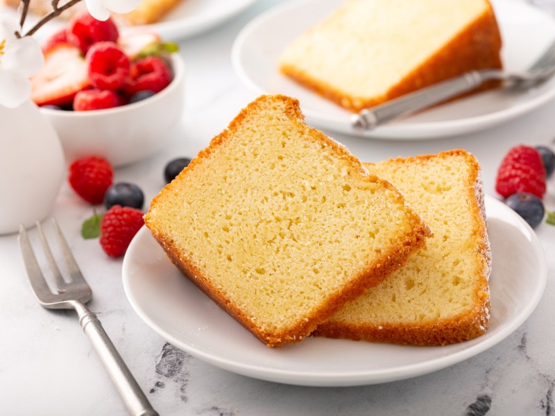 Zwei Stücke französischer Joghurtkuchen auf einem weißen Teller. Daneben liegen verschiedene Beeren.