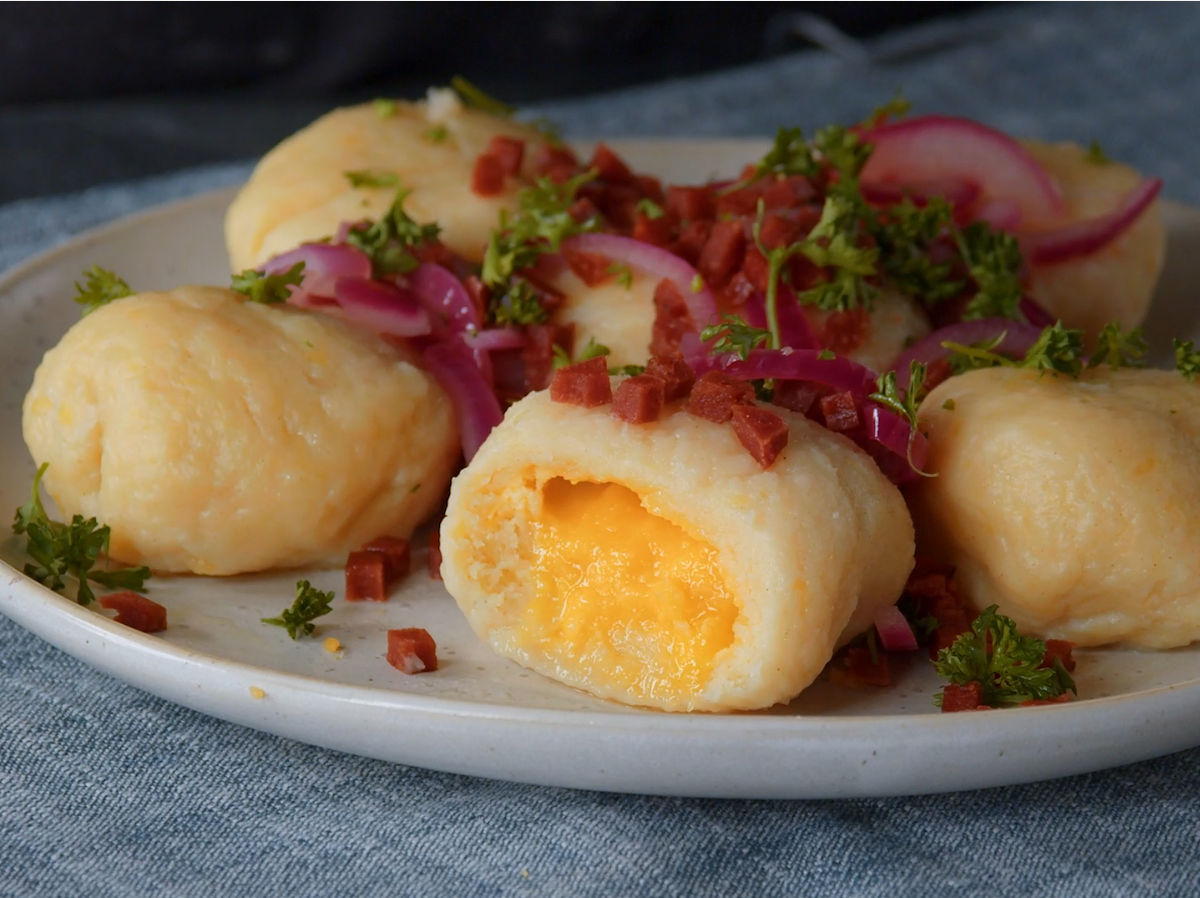 Ein angeschnittener Gnocchi mit Eifüllung auf einem Teller, garniert mit Zwiebeln, Petersilie und Speck