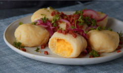 Ein angeschnittener Gnocchi mit Eifüllung auf einem Teller, garniert mit Zwiebeln, Petersilie und Speck