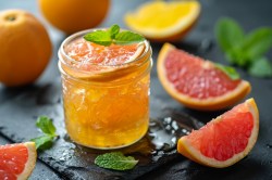 Ein Glas mit Grapefruit-Aperol-Marmelade und Grapefruitstücken daneben