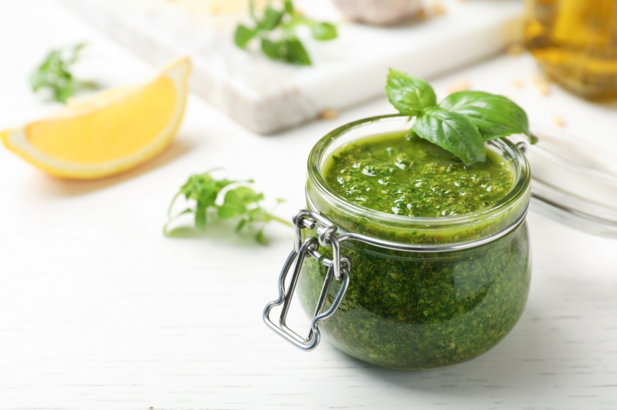 Ein Glas Basilikumpesto, ein grünes Pesto-Rezept, daneben eine Zitronenspalte und Basilikum.