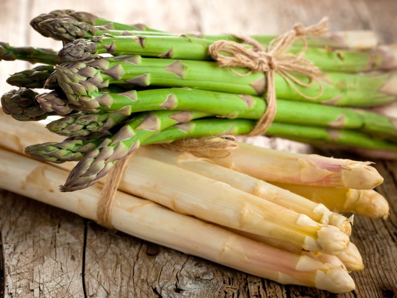 Grüner oder weißer Spargel gesünder: Ein Bund grüner Spargel liegt auf einem Bund weißem Spargel.