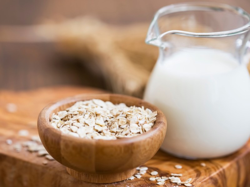 Ist Hafermilch gesund: Eine Glaskaraffe mit Hafermilch- daneben eine Schüssel Haferflocken.