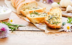 ein angeschnittenes selbst gemachtes Kräuterbaguette, daneben frische Wiesenblumen