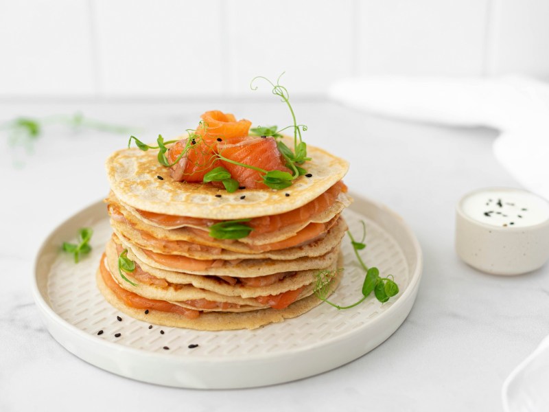 Teller mit Kräuter-Pancake mit Räucherlachs auf hellem Untergrund.