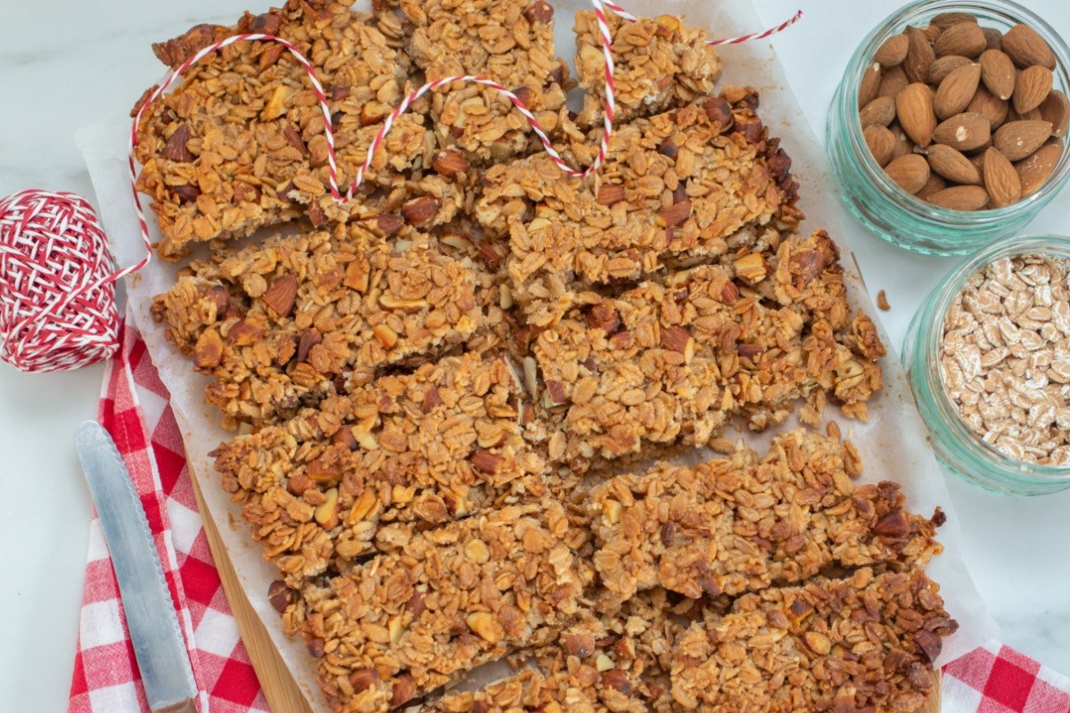 Müslikuchen in mehrere Stücke zerteilt, in der Draufsicht. Daneben stehen Schalen mit Mandeln und Haferflocken.