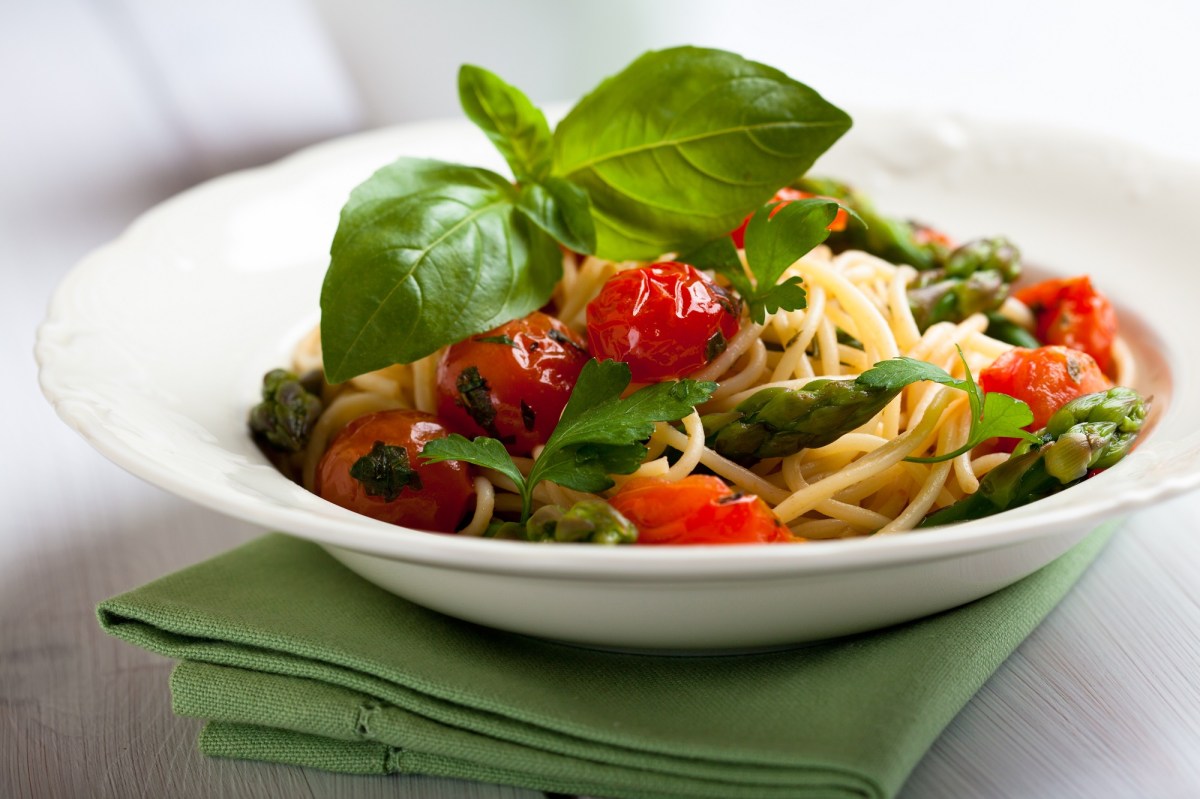 Teller mit Spaghetti mit geschmolzenen Tomaten und grünem Spargel.