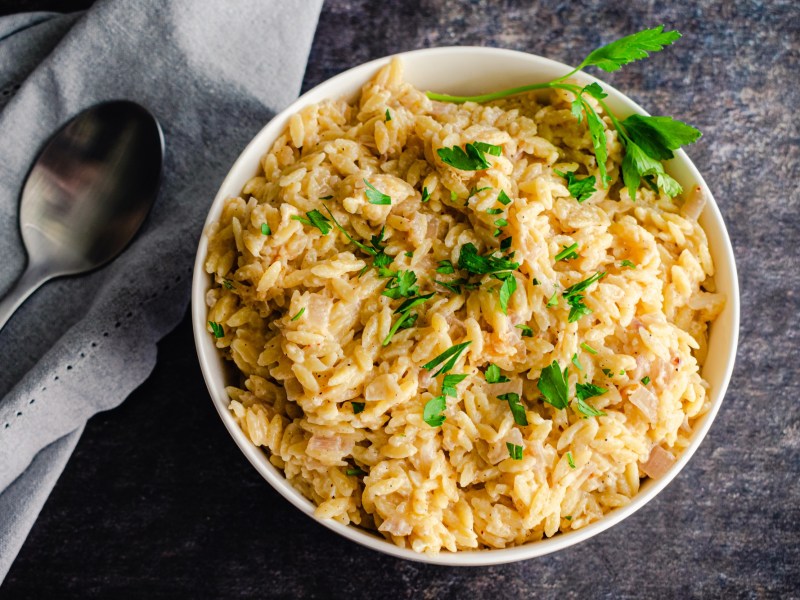 Ein Teller mit Parmesan-Orzo-Nudeln und Besteck auf grauem Tisch