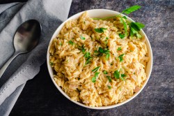 Ein Teller mit Parmesan-Orzo-Nudeln und Besteck auf grauem Tisch