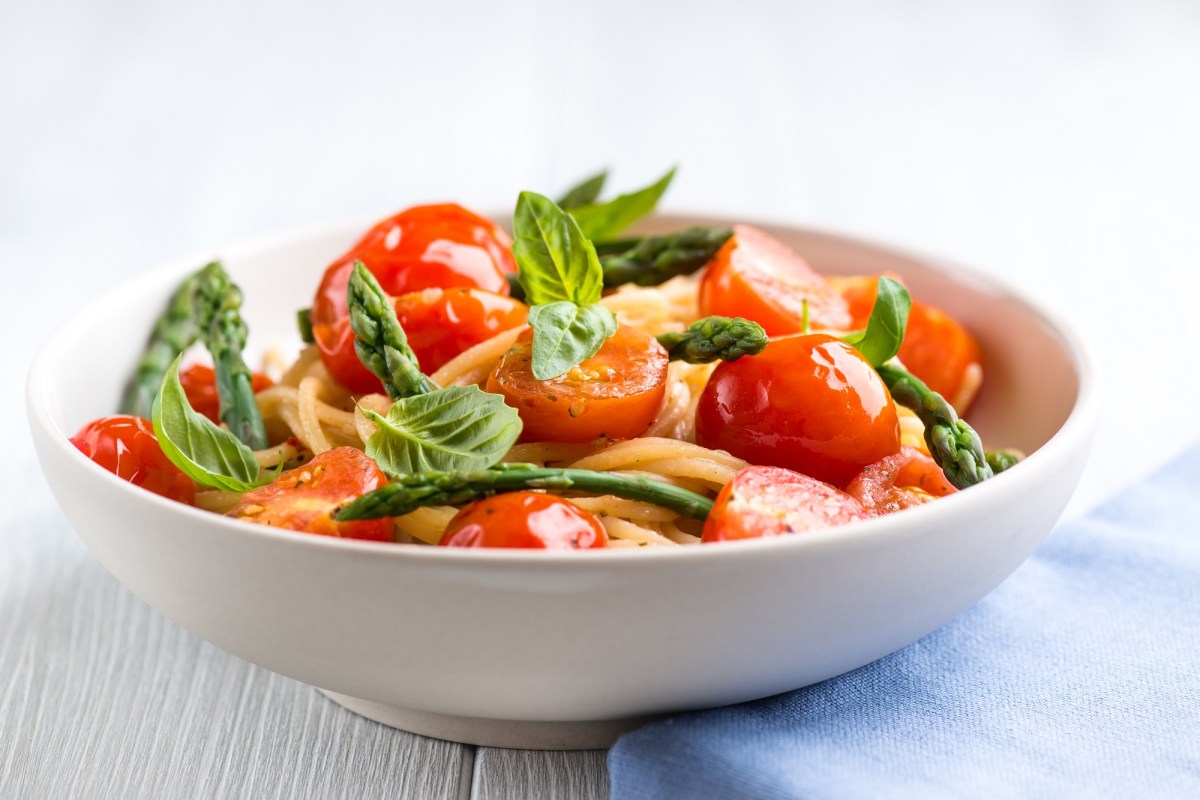 Spargel-Tomaten-Pasta in einer weißen Schüssel, dekoriert mit Basilikum.