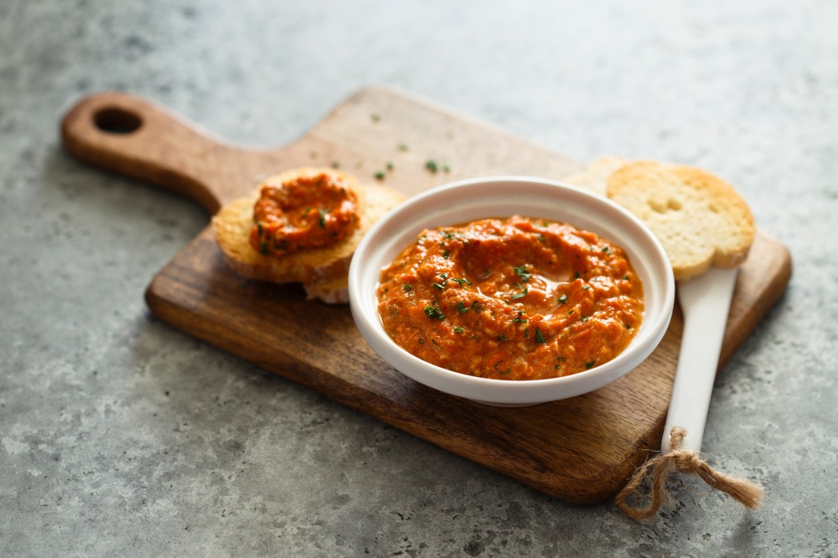 Pesto Calabrese in einer weißen Schale auf einem Holzbrett. Daneben liegt ein Stück Brot.