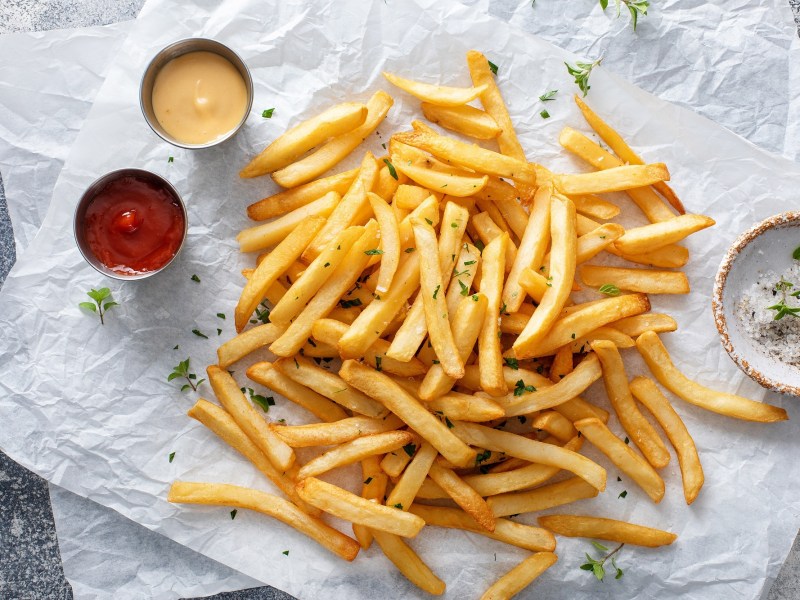 Pommes aufwärmen: Eine Portion Pommes mit Dips liegt auf Backpapier.