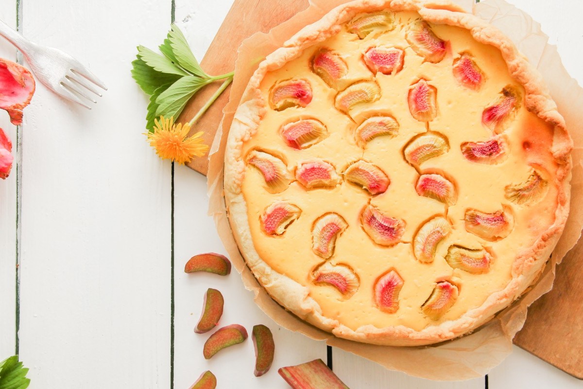 Ein Rhabarber-Quarkkuchen in der Draufsicht. Drumherum liegen Rhabarberstücke und -stangen.