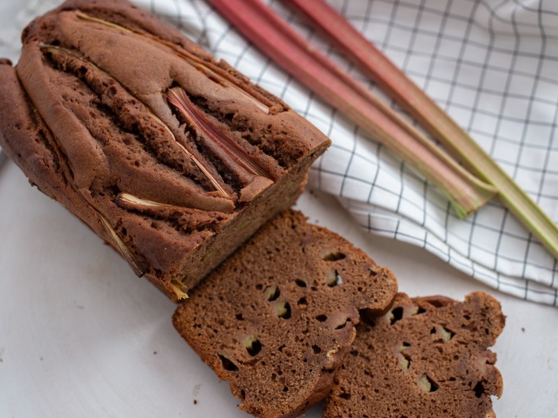 Aufgeschnittener Rhabarber-Schokokuchen mit zwei Stangen Rhabarber daneben.