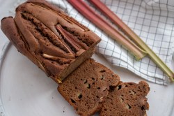 Aufgeschnittener Rhabarber-Schokokuchen mit zwei Stangen Rhabarber daneben.