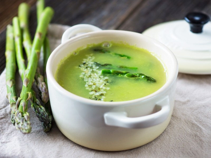 Kleiner Topf mit grüne Spargel Gazpacho und einem Bund Spargel daneben