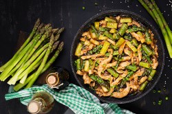 Asiatische Spargel-Hähnchen-Pfanne, daneben liegen Stangen grüner Spargel und einige Flaschen mit Soja- und Austernsoße