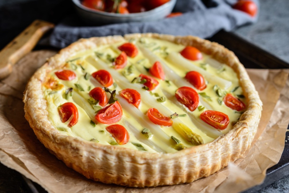 Eine Spargel-Tomaten-Tarte auf einem Stück Backpapier.