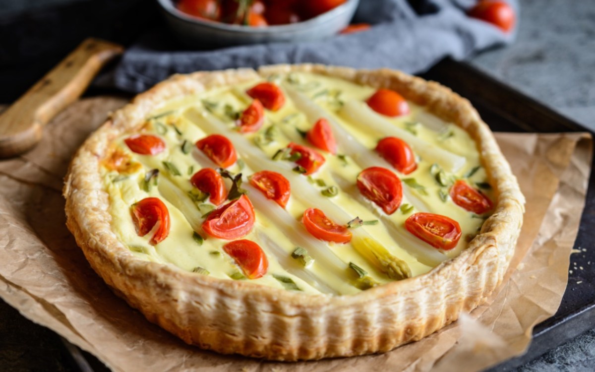 Eine Spargel-Tomaten-Tarte auf einem Stück Backpapier.