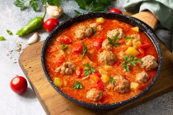 Tomatensuppe mit Hackbällchen in einer gusseisernen Pfanne, garniert mit Kräutern, daneben kleine Tomaten.