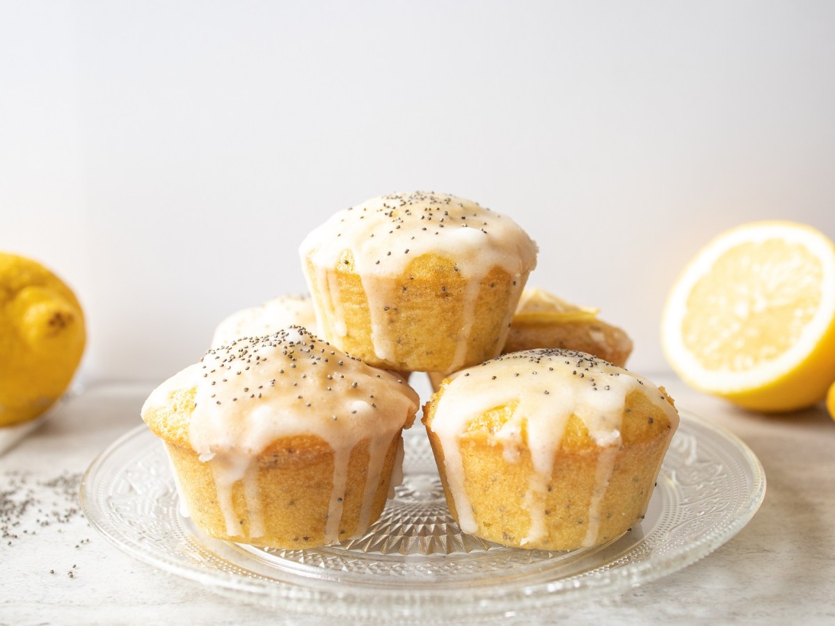 Glasplatte mit Zitronen-Mohn-Muffins und Zitronen im Hintergrund.