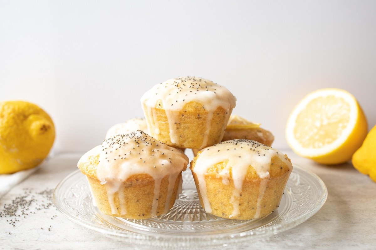 Glasplatte mit Zitronen-Mohn-Muffins und Zitronen im Hintergrund.