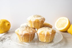 Glasplatte mit Zitronen-Mohn-Muffins und Zitronen im Hintergrund.