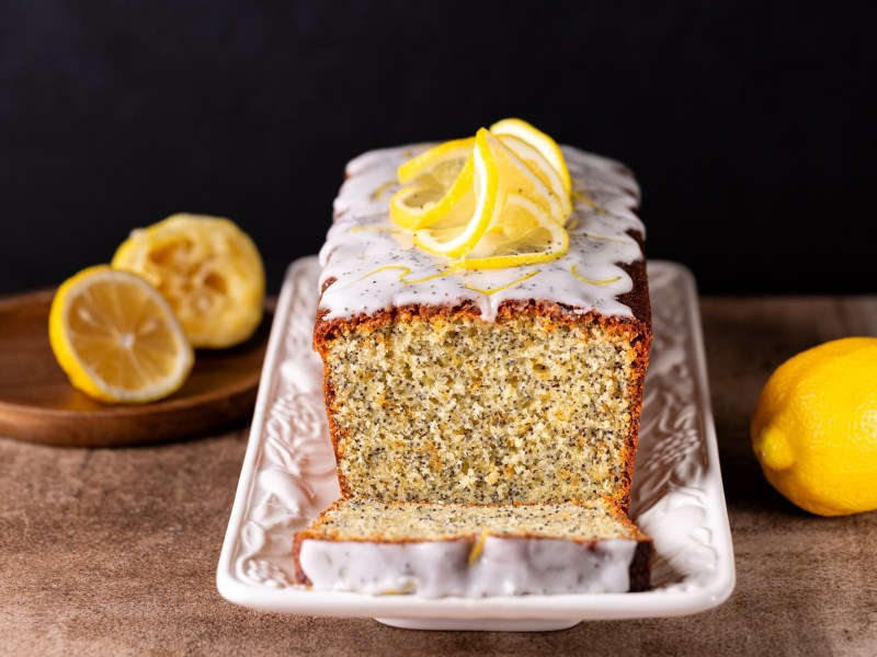 Ein angeschnittener und dekorierter Zitronen-Mohnkuchen mit Olivenöl.