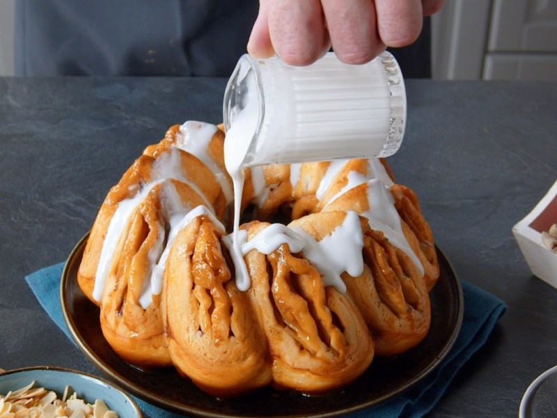 Apfelstrudel-Kuchen, der mit Zuckerguss übergossen wird.