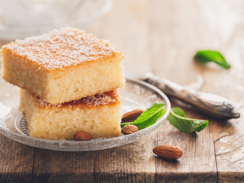 Basbousa, arabischer Gewürzkuchen auf einem Glasteller. Daneben liegen Mandeln und etwas Minze.