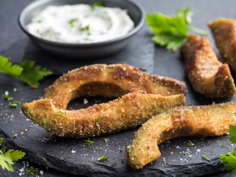 Frittierte Avocado auf schwarzem Teller mit Kräuter-Dip.