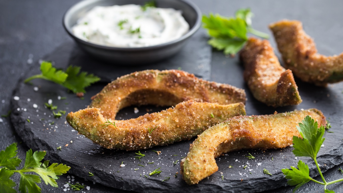 Frittierte Avocado auf schwarzem Teller mit Kräuter-Dip.