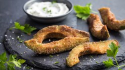 Frittierte Avocado auf schwarzem Teller mit Kräuter-Dip.