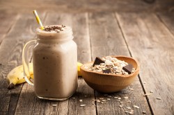 Glas mit Bananen-Schokoladen-Smoothie, Schale mit Haferflocken daneben