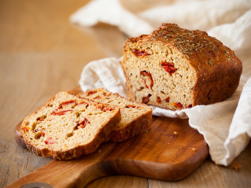 Brot mit getrockneten Tomaten auf einem Tuch, das auf einem Holzbrett liegt.