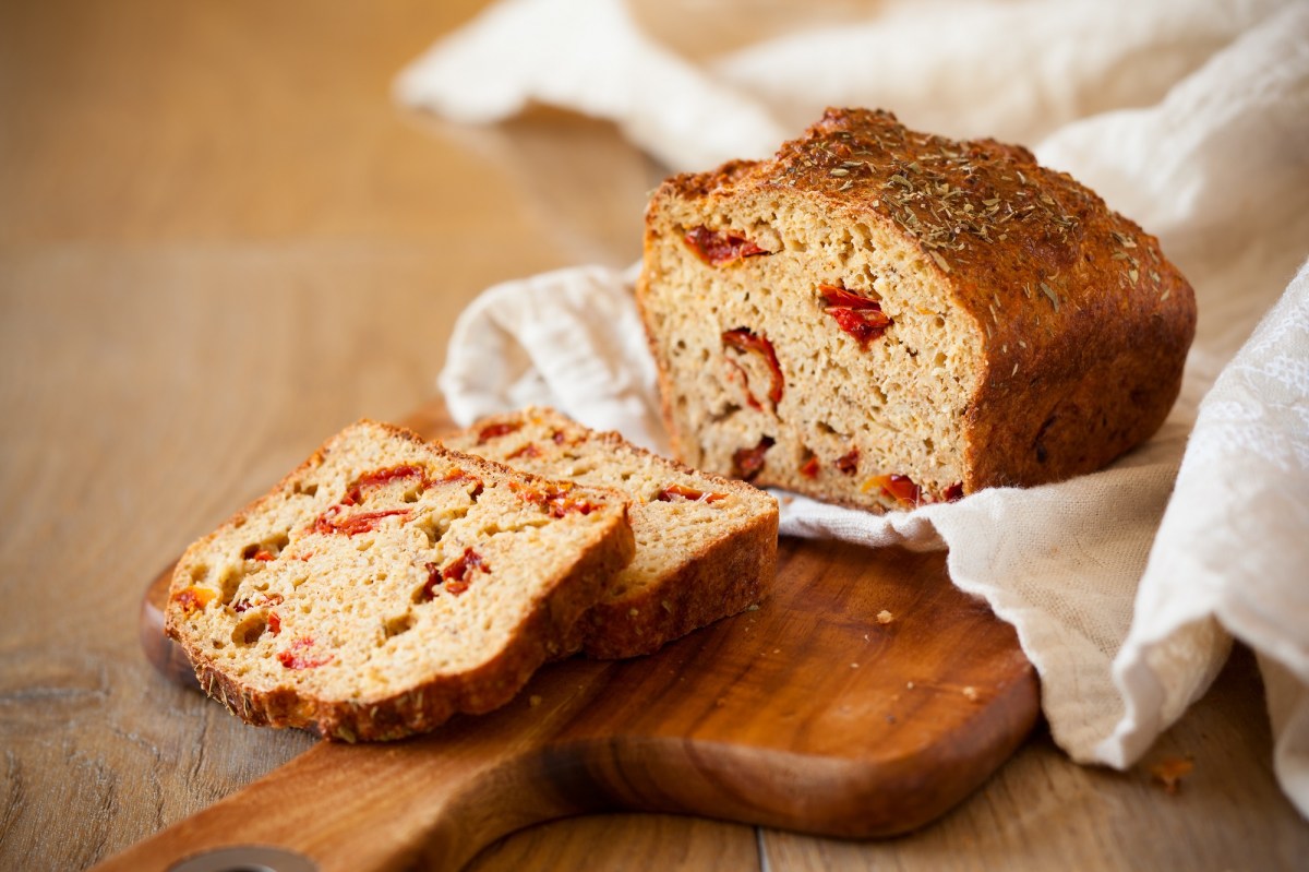 Brot mit getrockneten Tomaten auf einem Tuch, das auf einem Holzbrett liegt.