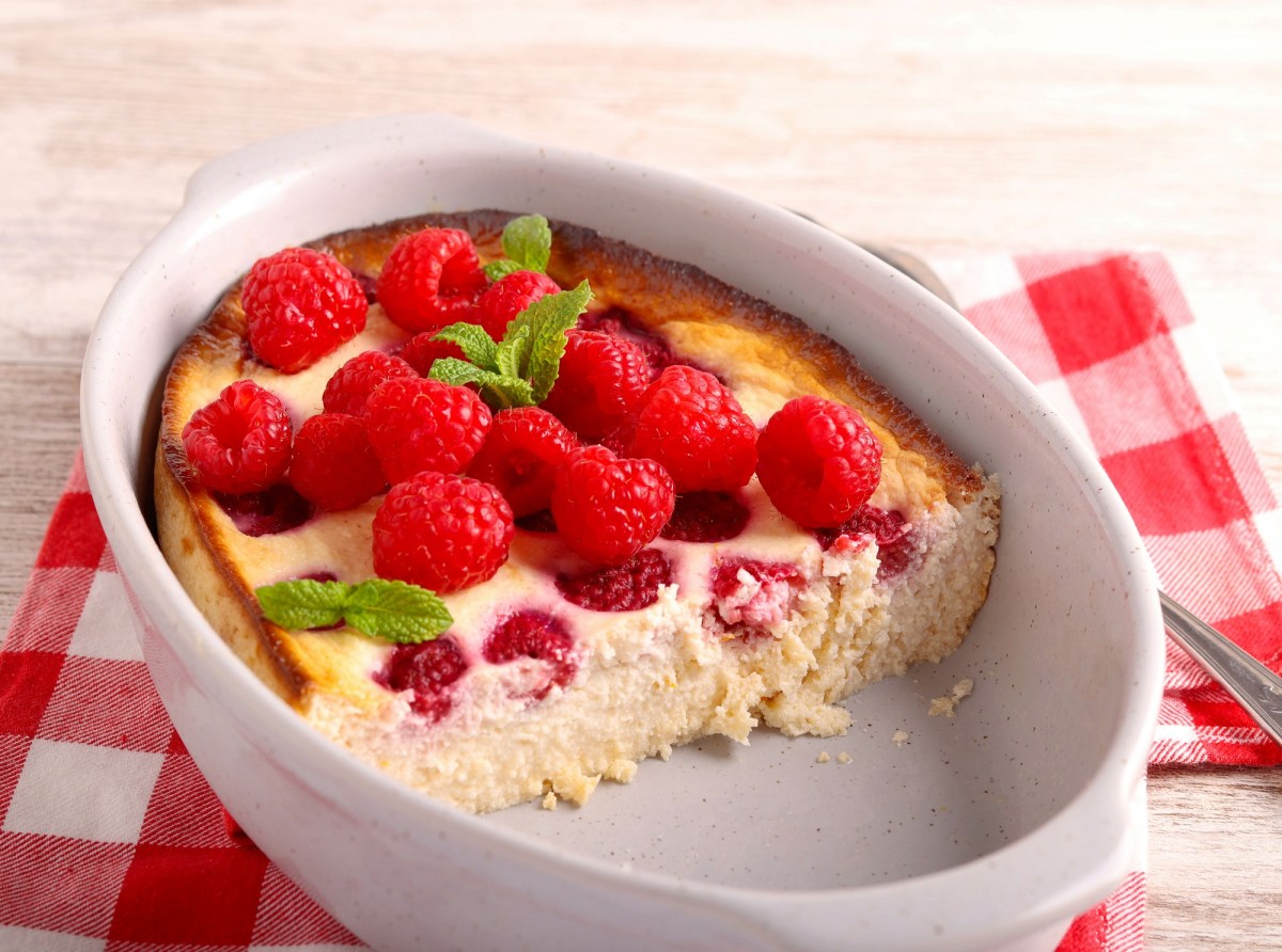 ein halber Cheesecake-Auflauf mit Himbeeren in ovaler Auflaufform, die auf rot-weiß kariertem Deckchen steht.